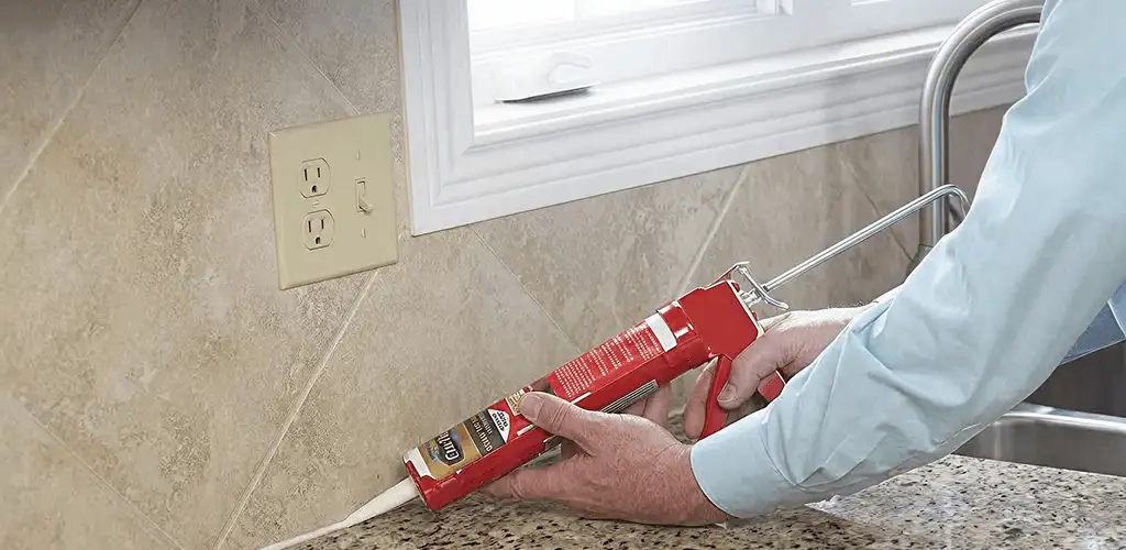 Handyman applying caulk along a kitchen backsplash and countertop seam in Ann Arbor, MI