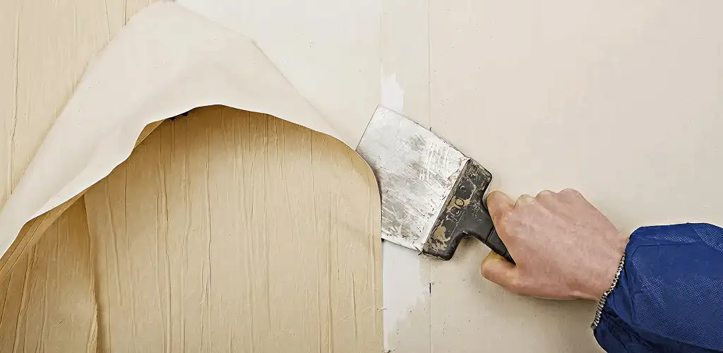 Handyman removing wallpaper with a scraper for wall preparation in Ann Arbor, MI